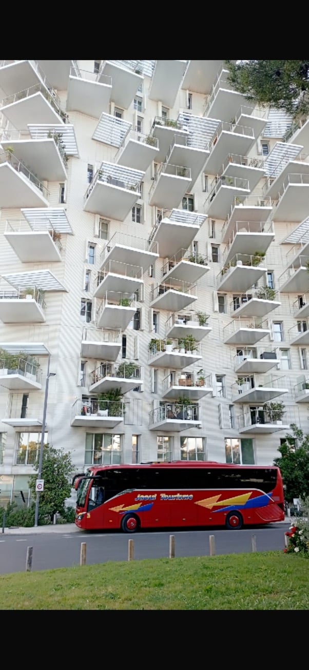 Architecture moderne aux balcons blancs saillants devant un bus rouge Jacoul Tourisme à Montpellier.