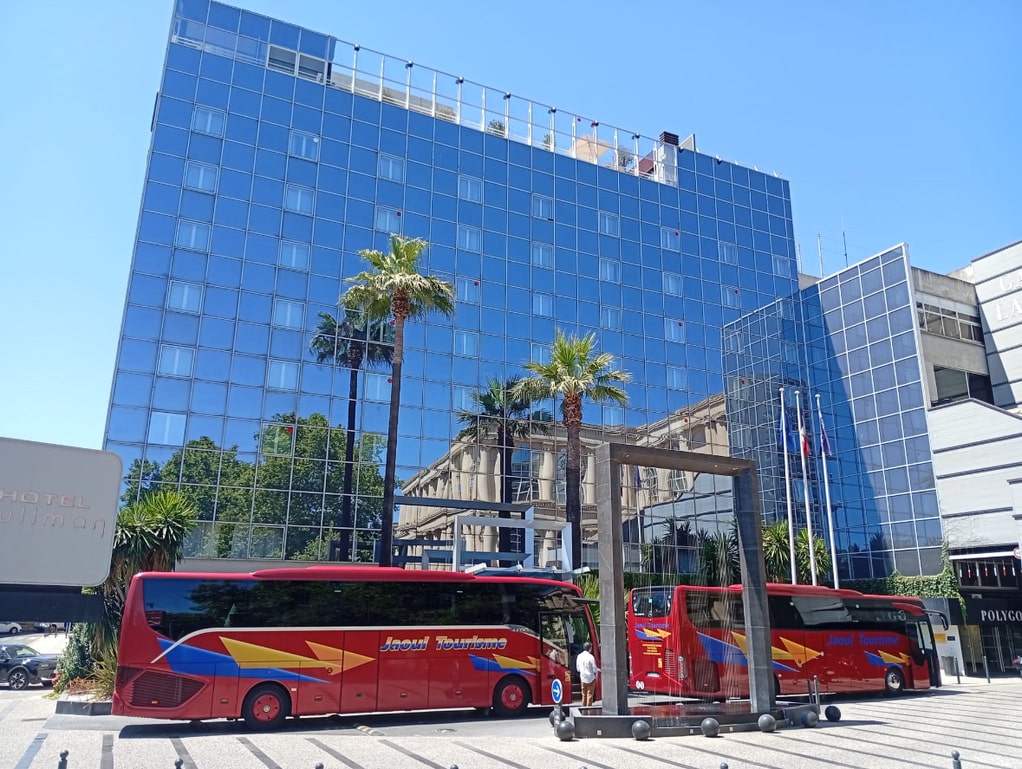 Hôtel Pullman à façade bleue et bus Jaoul Tourisme devant des palmiers.