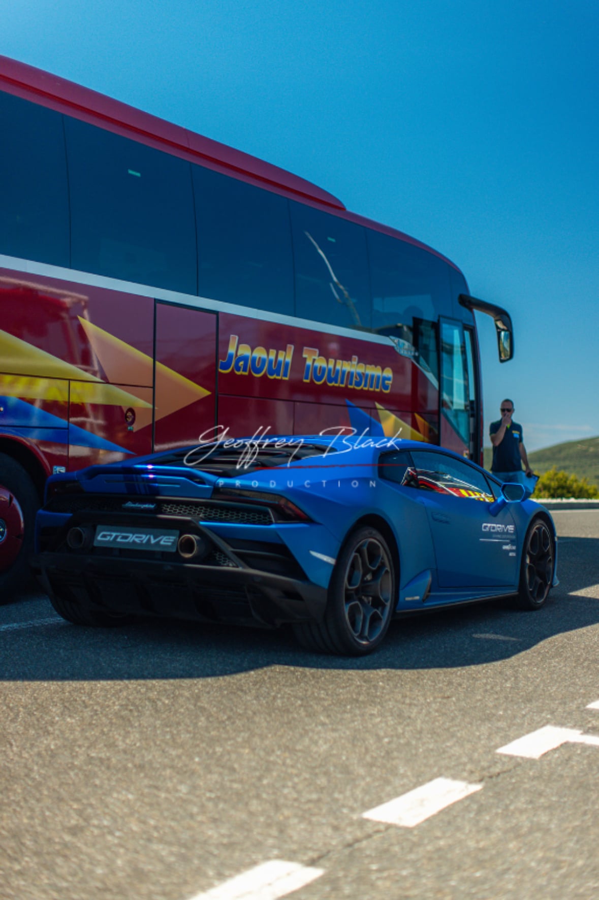 Lamborghini bleue GTDRIVE garée devant un car Jaoul Tourisme sous un ciel dégagé.
